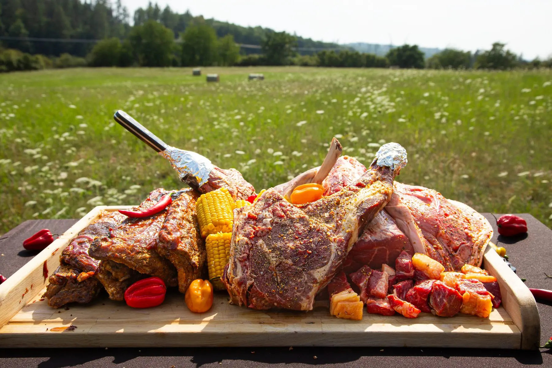 BBQ — a board full of tomahawks, ribs and corn in a meadow