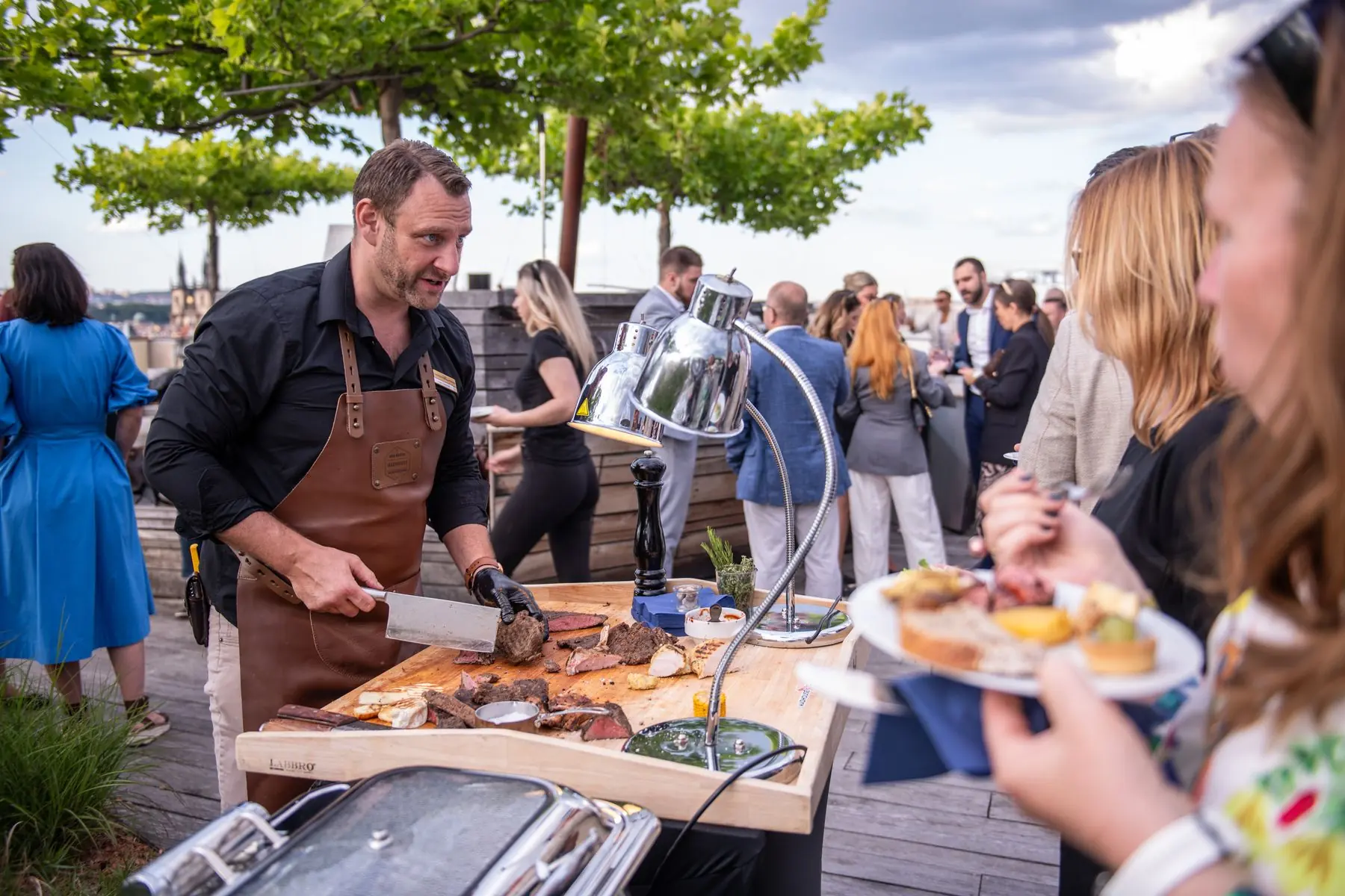 Honza carving meat for guests at a corporate event on a Prague rooftop
